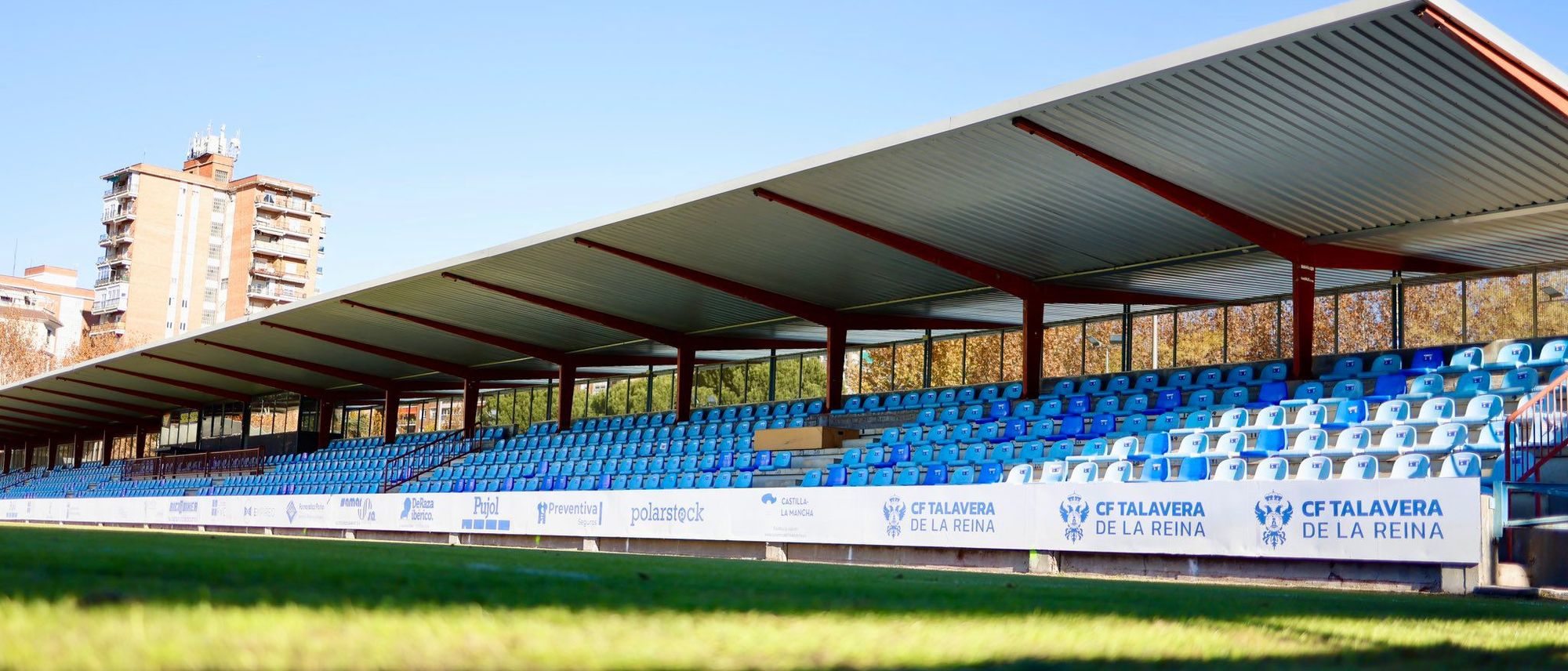 Tribuna cubierta con butacas azules a ras de césped